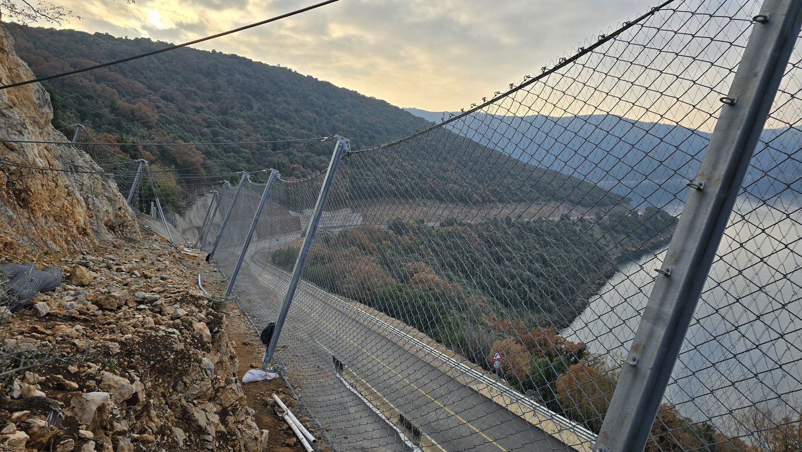 Rockfall protection system with ropes and wire mesh on the slope above a harbour road, road and sea below