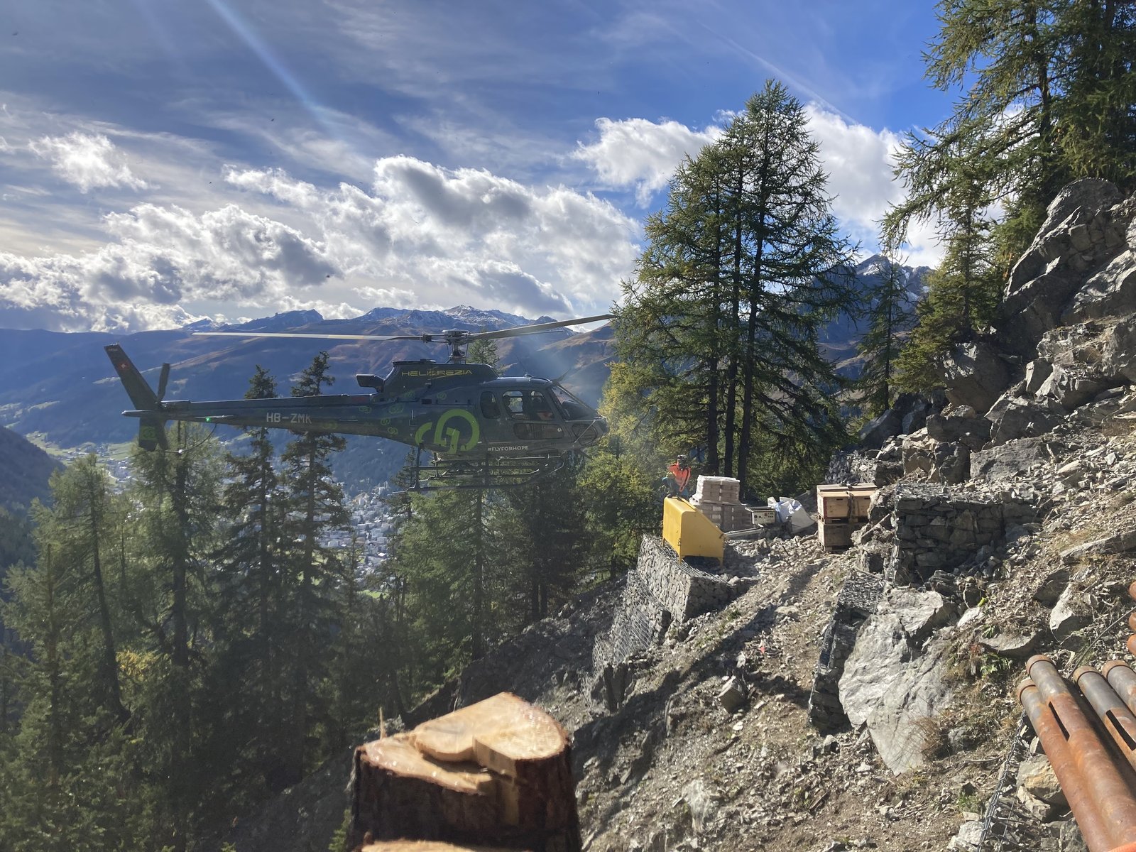 Helicopter transporting material for installation work on a steep slope, the Alps behind
